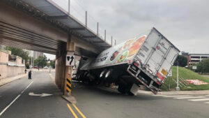 A truck accident leaves the truck stuck on a bridge at a semi-overturned angle, causing property damage.