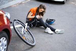 A woman suffered a bicycle accident. She is on the floor with the bike between her legs and she is trying to get up