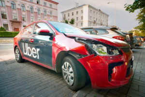 The front of a red car was crashed and is destroyed. The word UBER can be clearly seen on the car door.